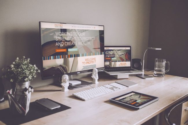 picture of a desk with a computer and iPad displaying the website by protect commercial